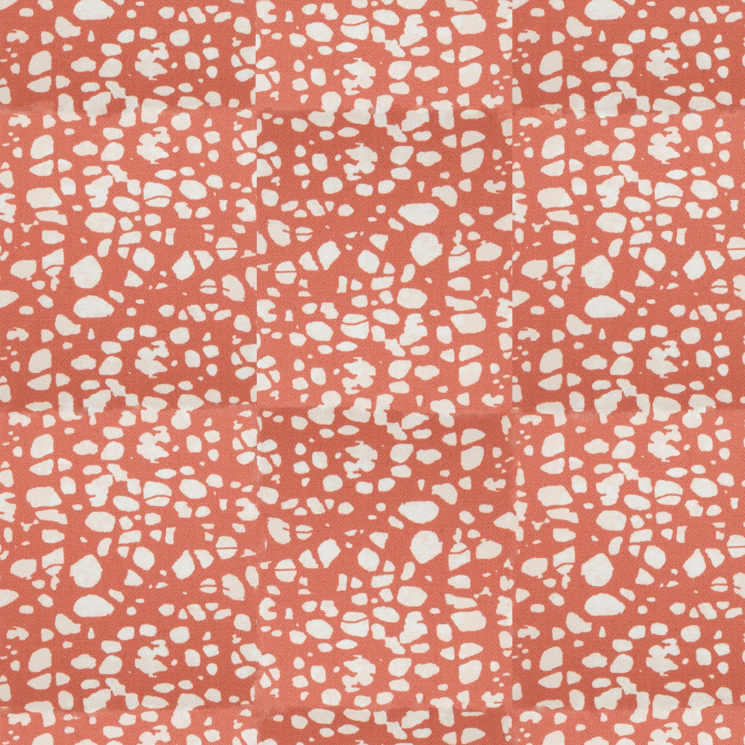 Detail of fabric in a batik splatter print in cream on a coral field.