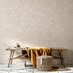 A bench and basket stand in front of a wall papered in a painterly botanical print in white and light pink on a cream field.