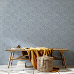 A bench and basket stand in front of a wall papered in a painterly abstract print in white on a light blue field.