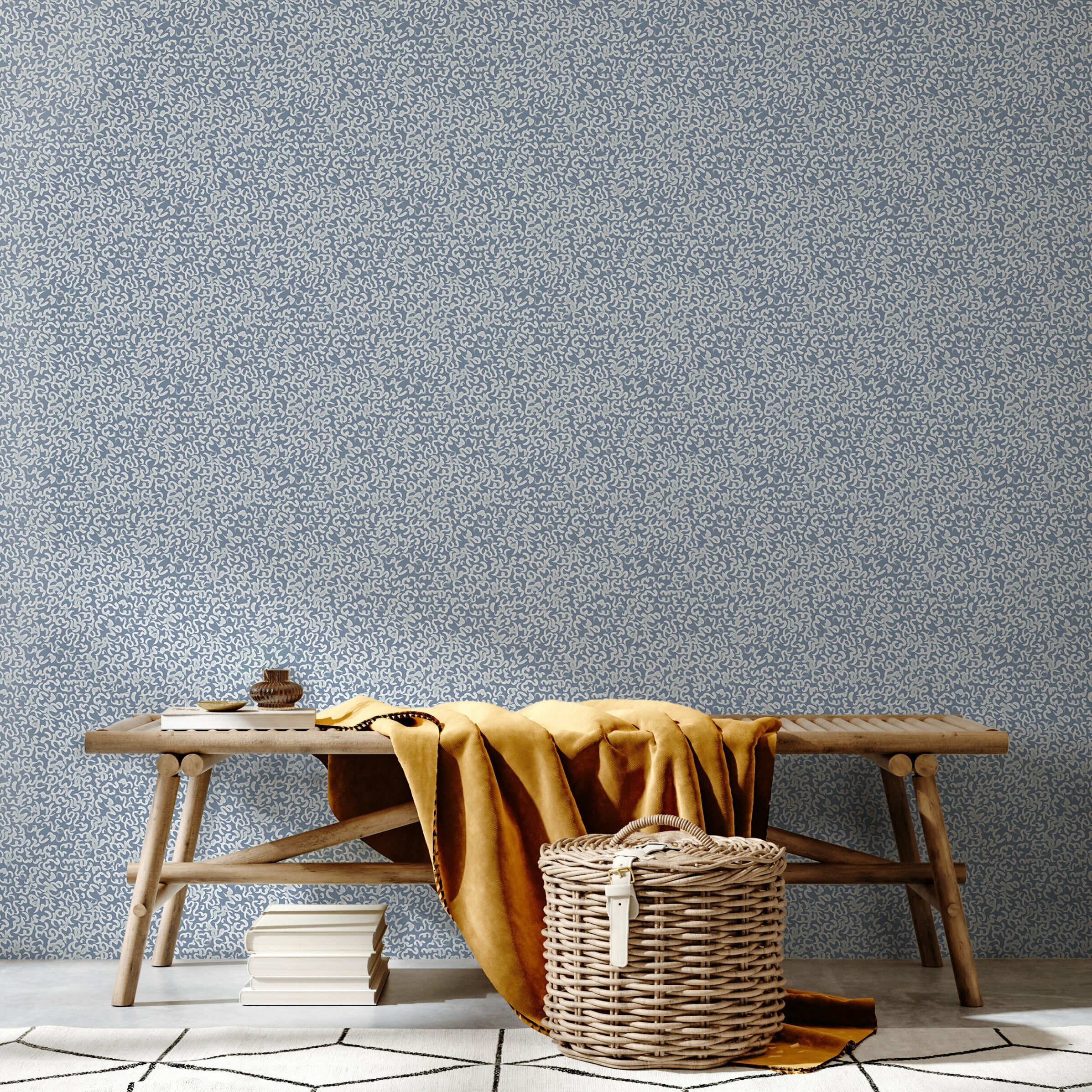 A bench and basket stand in front of a wall papered in a painterly abstract print in white on a light blue field.