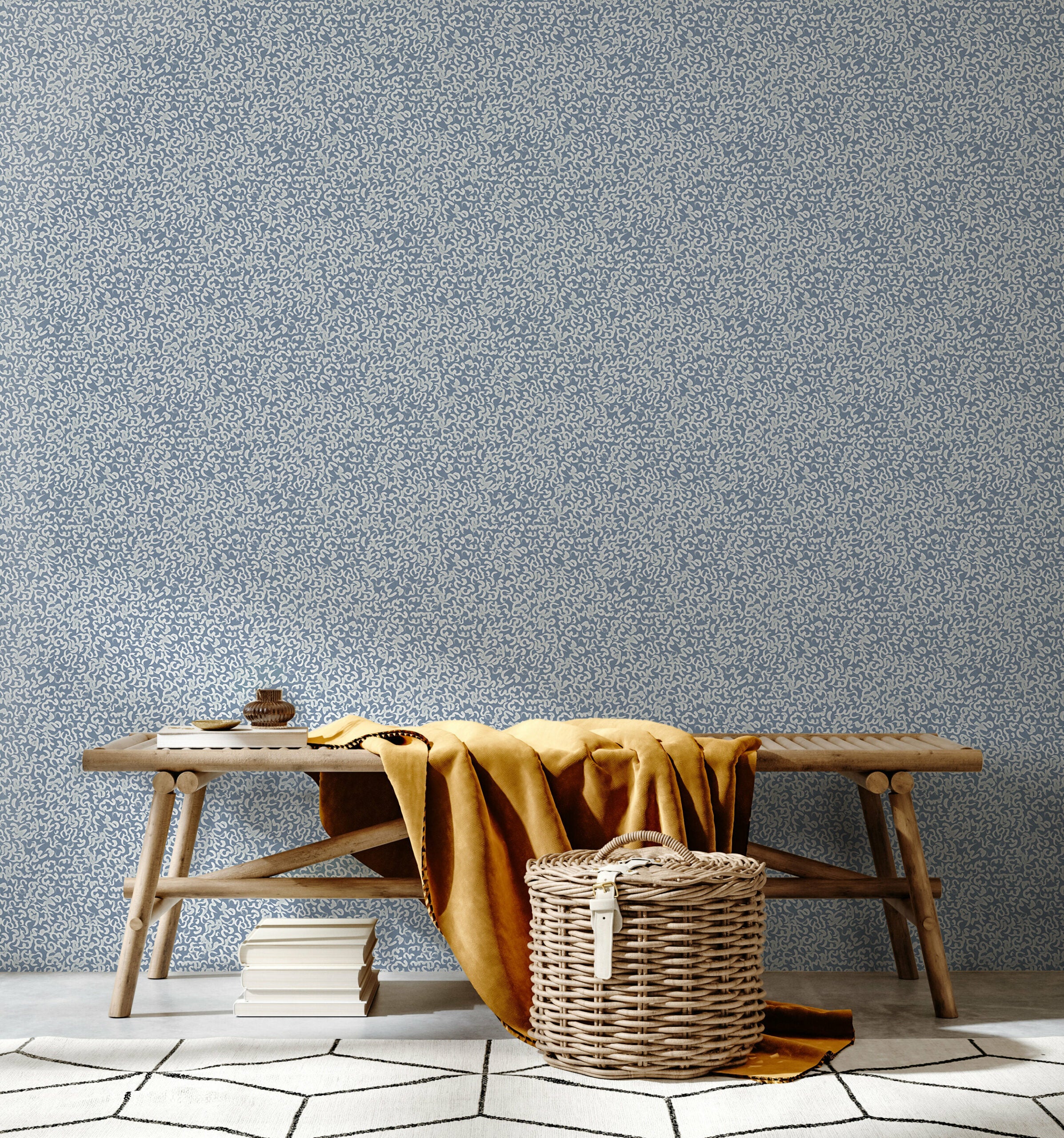 A bench and basket stand in front of a wall papered in a painterly abstract print in white on a light blue field.