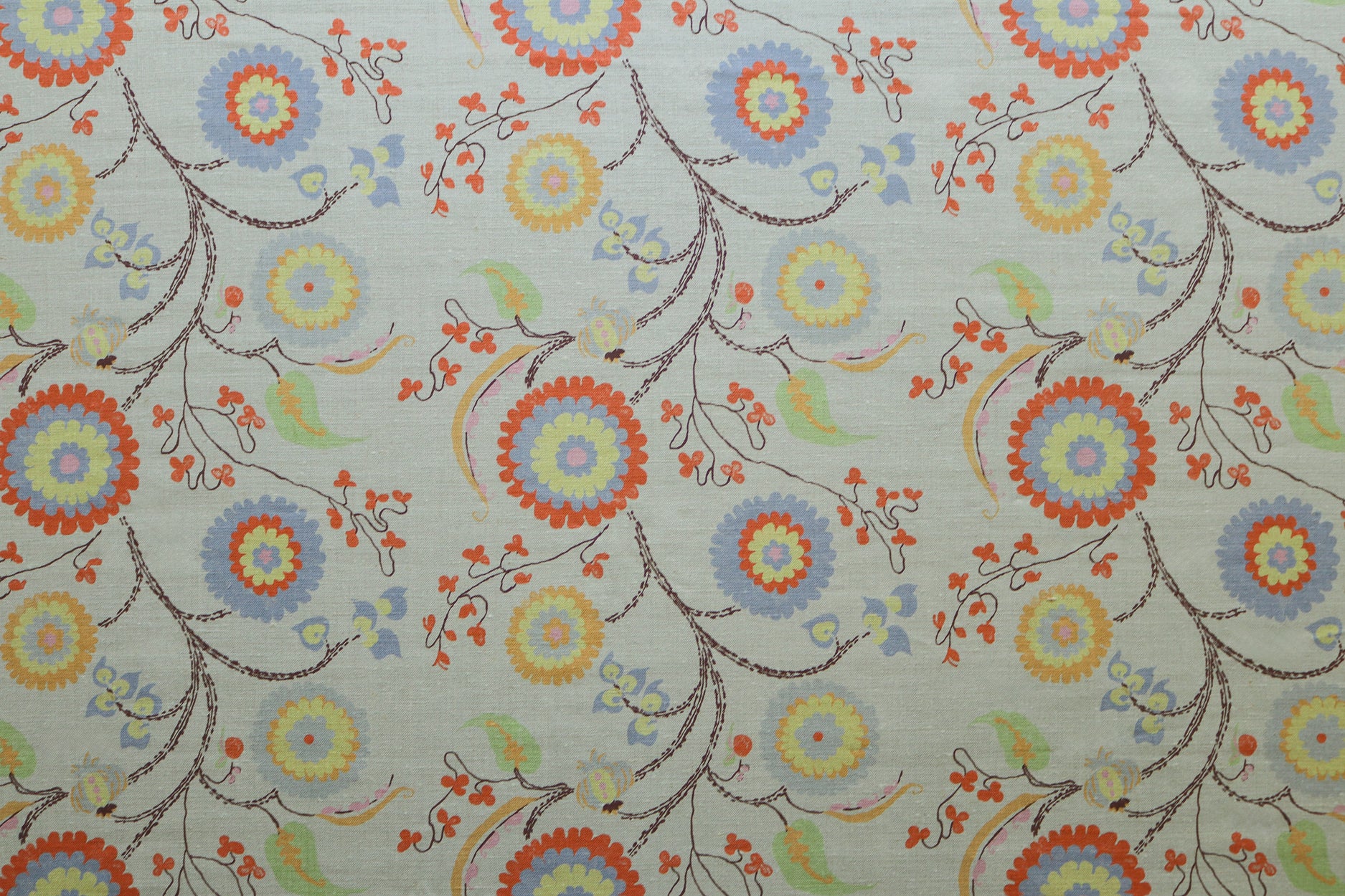 Printed fabric with a whimsical floral pattern in blue, yellow and orange with dark brown stems on a soft blue background. 