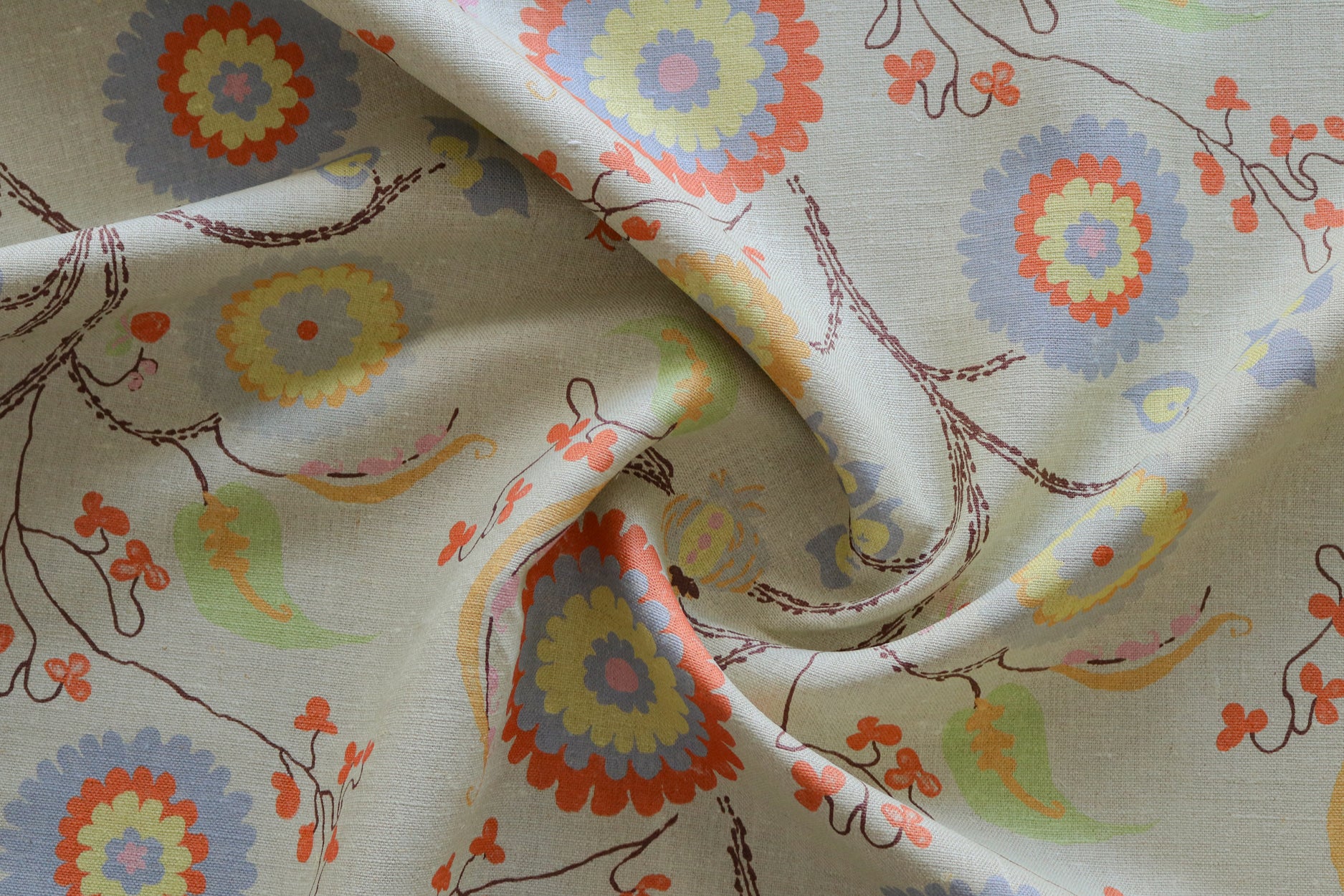Close up of gently draped printed fabric with a whimsical floral pattern in blue, yellow and orange with dark brown stems on a soft blue background. 