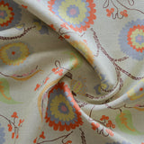 Close up of gently draped printed fabric with a whimsical floral pattern in blue, yellow and orange with dark brown stems on a soft blue background. 