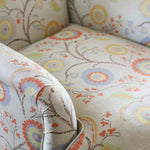Close-up of a upholstered armchair with rolled arms and a cream fabric covered in a multicolor floral and vine pattern.