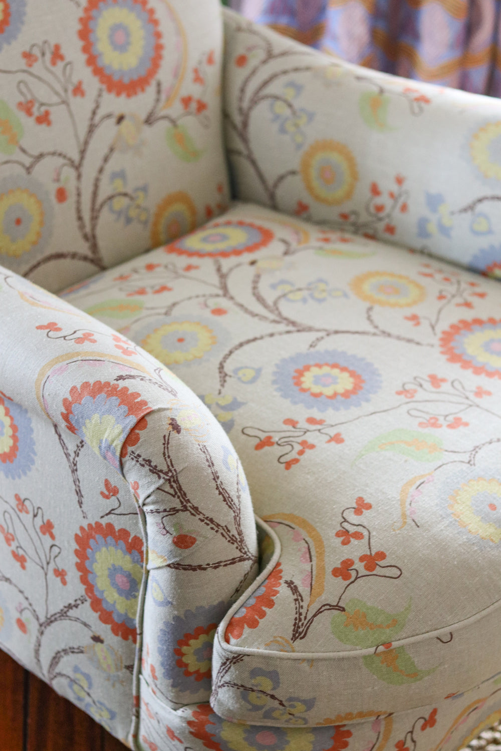 Close-up of a upholstered armchair with rolled arms and a cream fabric covered in a multicolor floral and vine pattern.