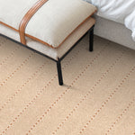 Bedroom detail with an upholstered linen bench over a herringbone stripe carpet in ecru and brown.