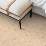 Bedroom detail with an upholstered linen bench over a herringbone stripe carpet in ecru and brown.