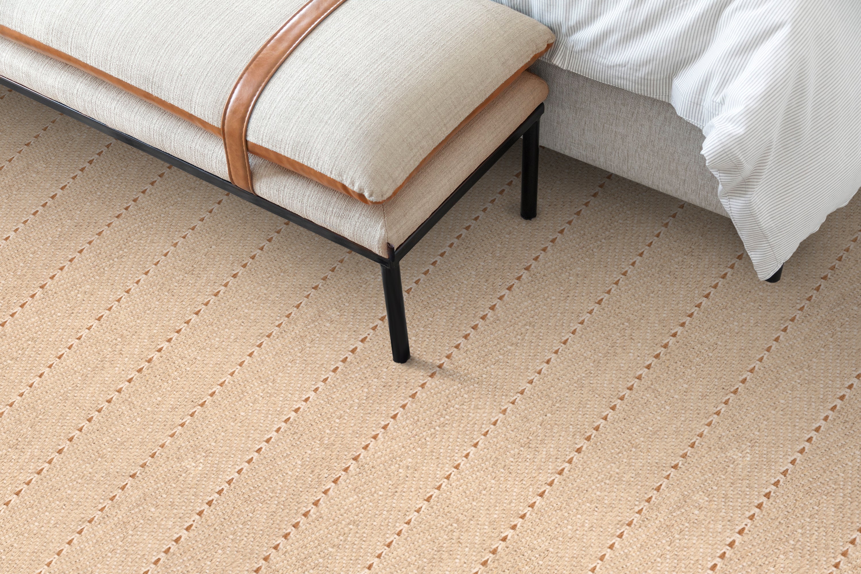 Bedroom detail with an upholstered linen bench over a herringbone stripe carpet in ecru and brown.