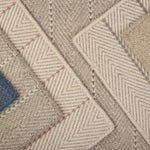 Stack of broadloom carpet samples in a striped herringbone design in an array of netural colors with accents of blue, pink, brown, green and grey. 