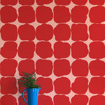 A vase of flowers stands in front of a wall papered in a repeating blot print in red on a pink field.