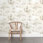 A wooden chair stands in front of a wall papered in a painterly bird and branch print in shades of brown, white and cream.