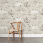 A wooden chair stands in front of a wall papered in a painterly bird and branch print in shades of gray, brown and cream.