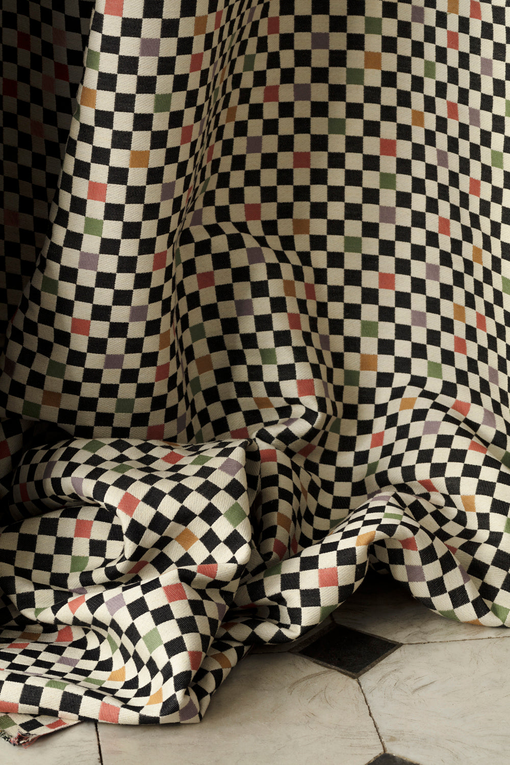 Draped jacquard fabric in a checked pattern in shades of yellow, pink, purple and black on a tan field.
