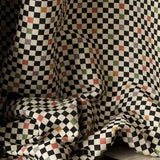 Draped jacquard fabric in a checked pattern in shades of yellow, pink, purple and black on a tan field.