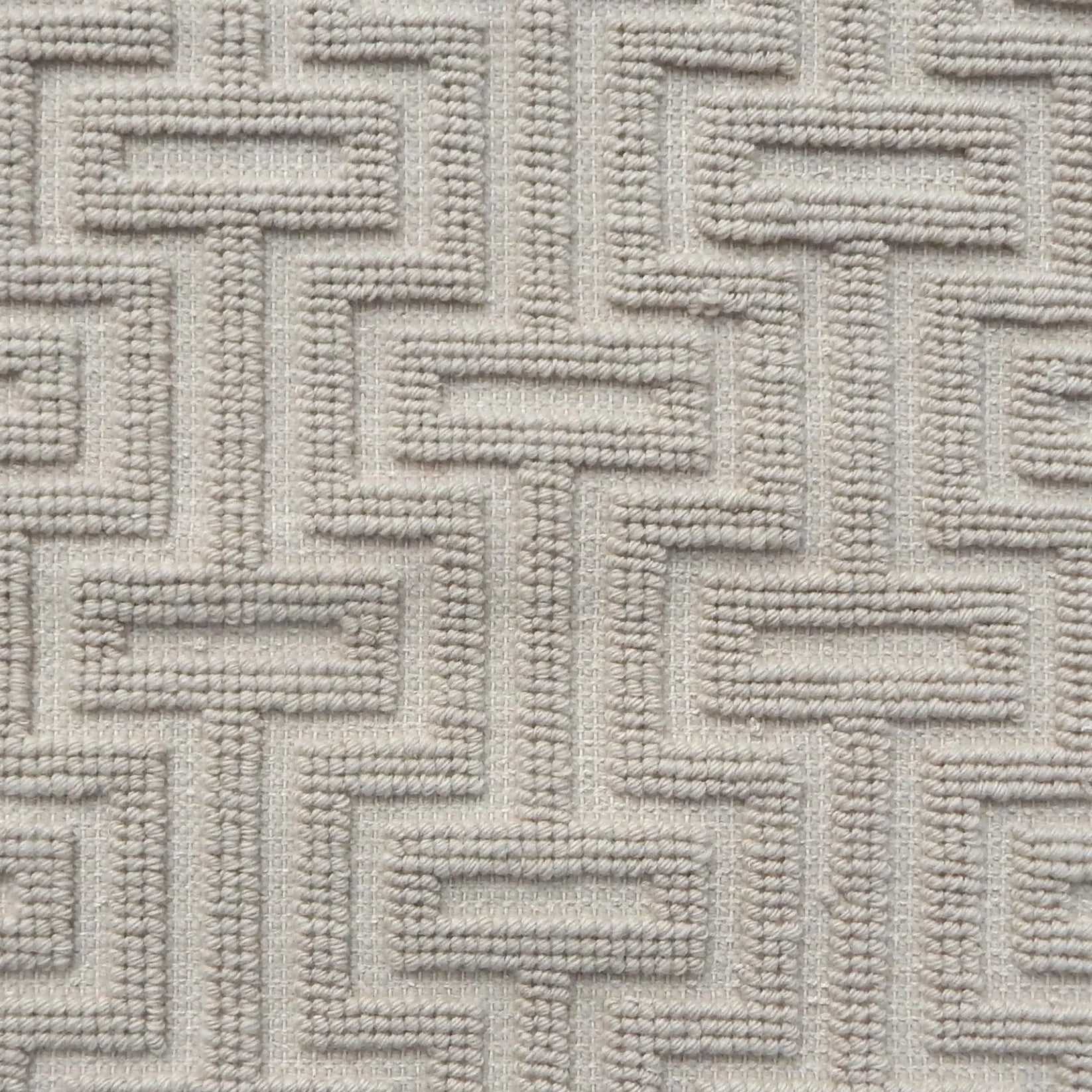 A close-up of a handwoven carpet with a repeating geometric maze in off white. 