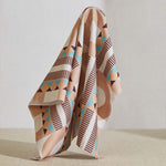 A large piece of draped fabric in a dense geometric print in shades of peach, blue and purple on a white field.