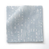 Stacked fabric swatches in a painterly small-scale dashed dot print in white on a soft blue watercolor field.