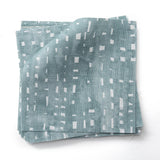 Stacked  fabric swatches in a painterly small-scale dashed dot print in white on a soft peacock blue watercolor field.