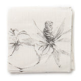A stack of fabric swatches in a painterly pine cone and branch print in green on a cream field.