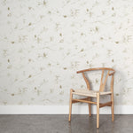 A wooden chair stands in front of a wall papered in a painterly pine cone and branch print in green on a cream field.