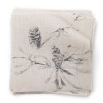 A stack of fabric swatches in a painterly pine cone and branch print in gray on a greige field.