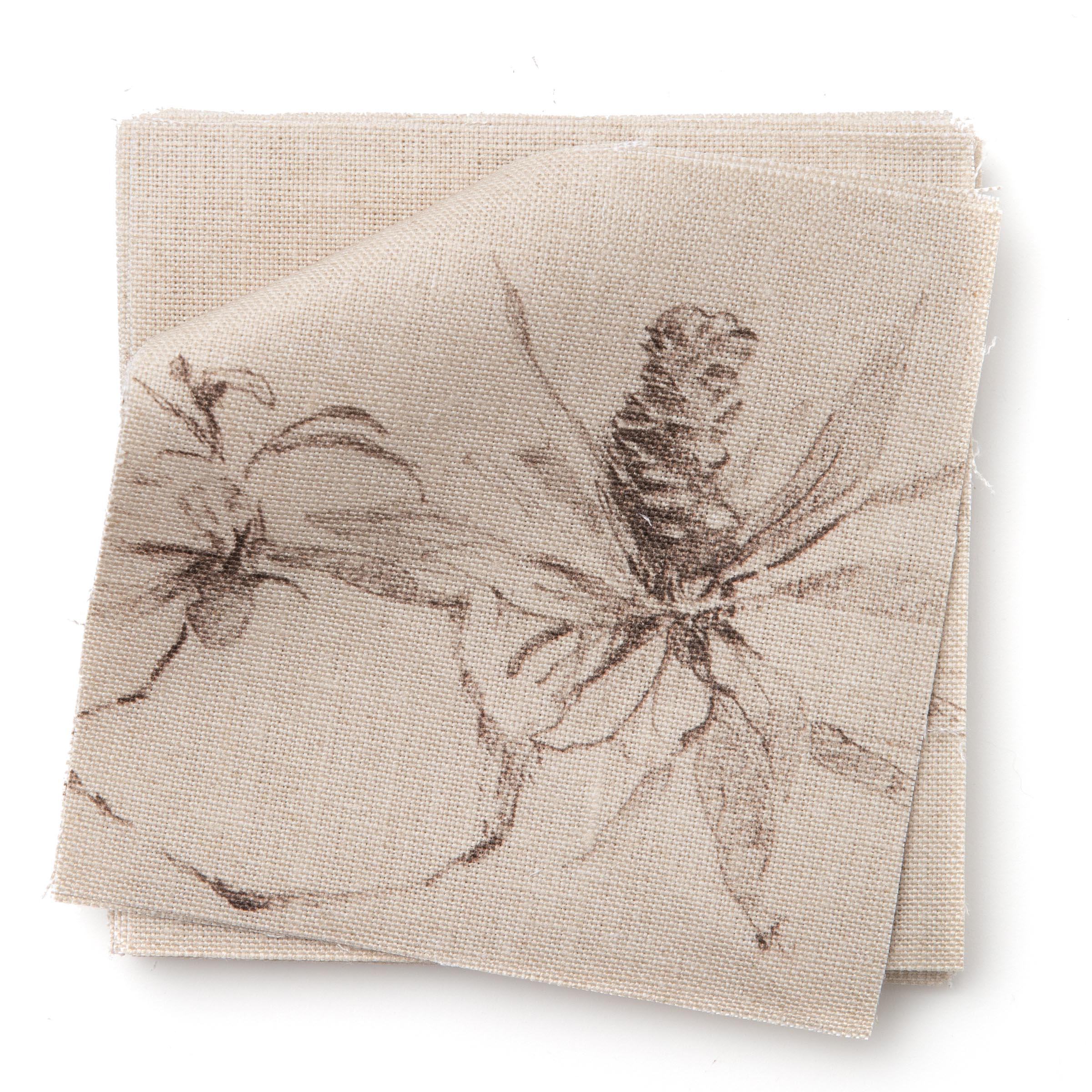 A stack of fabric swatches in a painterly pine cone and branch print in brown on a cream field.