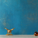 A table with knick knacks stands in front of a wall papered in a random splattered pattern in metallic gold on a blue field.