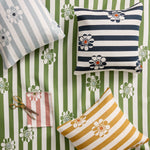 Three decorative throw pillows with striped and floral patterns are arranged on a green and white striped fabric background, alongside a small pair of scissors and a folded matching fabric swatch.