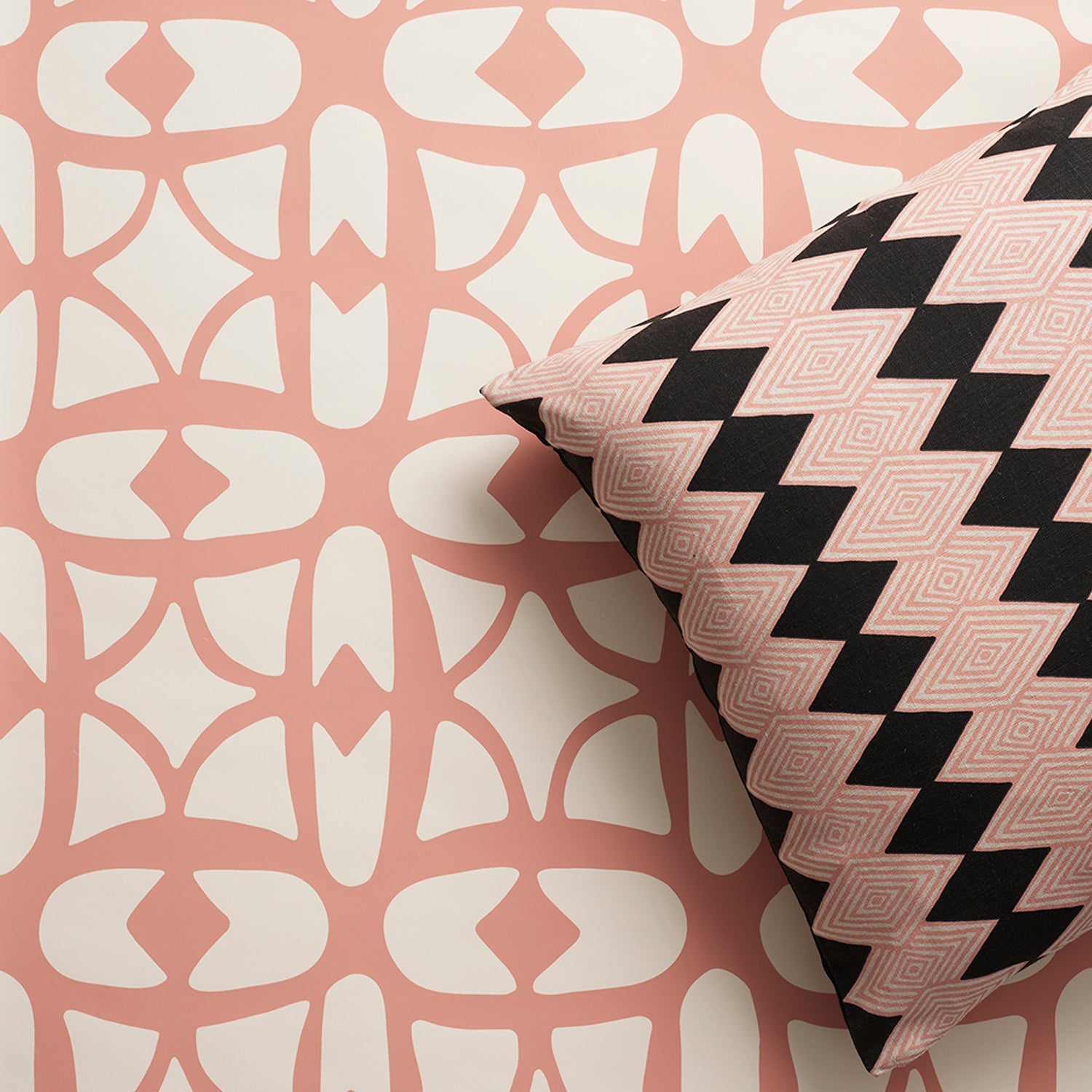 A close-up of a decorative throw pillow with a black and pink diamond stripe pattern, resting against a wallpaper with a pink and white lattice design.
