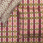A close-up of a woven-texture throw pillow and matching pillowcase set on a bed. The pillow features a pink, burgundy, and olive green basketweave pattern, while the matching pillowcase has a leopard print design in cream and burgundy.