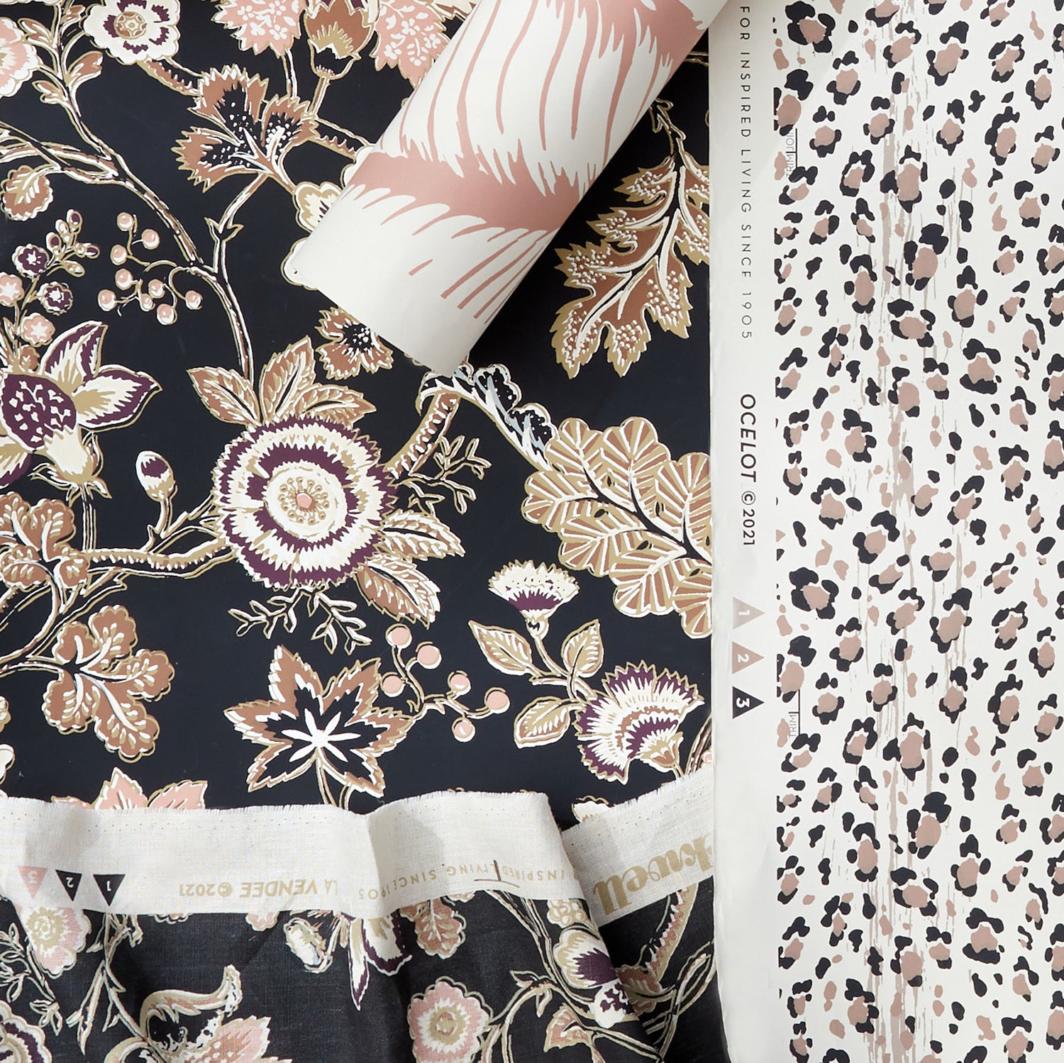 Styled flat-lay featuring a dark floral vine pattern in fabric and wallpaper paired with a roll of tropical print wallpaper in blush and white layered over a black and blush pink leopard print wallpaper. 