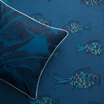 Styled flatlay with a dark blue banana leaf throw pillow atop a playful fish wallpaper in dark blue. 