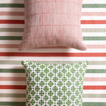 Styled flat-lay with bamboo striped pillow in pink and a white and green floral medallion patterned pillow on a striped fabric with white, green, red and pink. 
