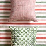 Styled flat-lay with bamboo striped pillow in pink and a white and green floral medallion patterned pillow on a striped fabric with white, green, red and pink. 