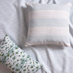 Two pillows on a pale blue fabric, one with a bold blue and white stripes and the other with a blue, green and white leopard pattern.