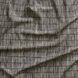 Close up of gently draped printed linen with thin hand drawn stripe grid in ivory on black.