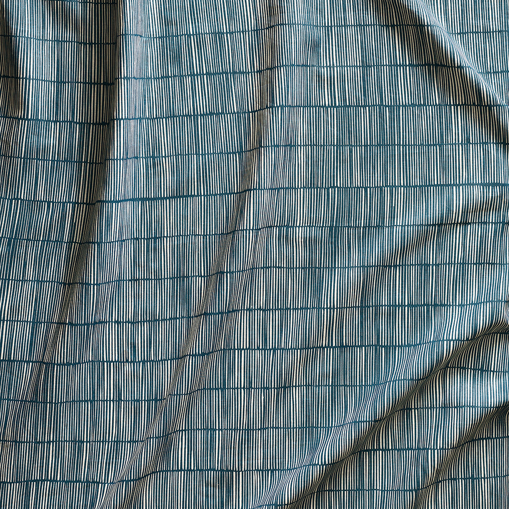 Close up of gently draped printed linen with thin hand drawn stripe grid in ivory on dark blue.