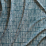 Close up of gently draped printed linen with thin hand drawn stripe grid in ivory on dark blue.
