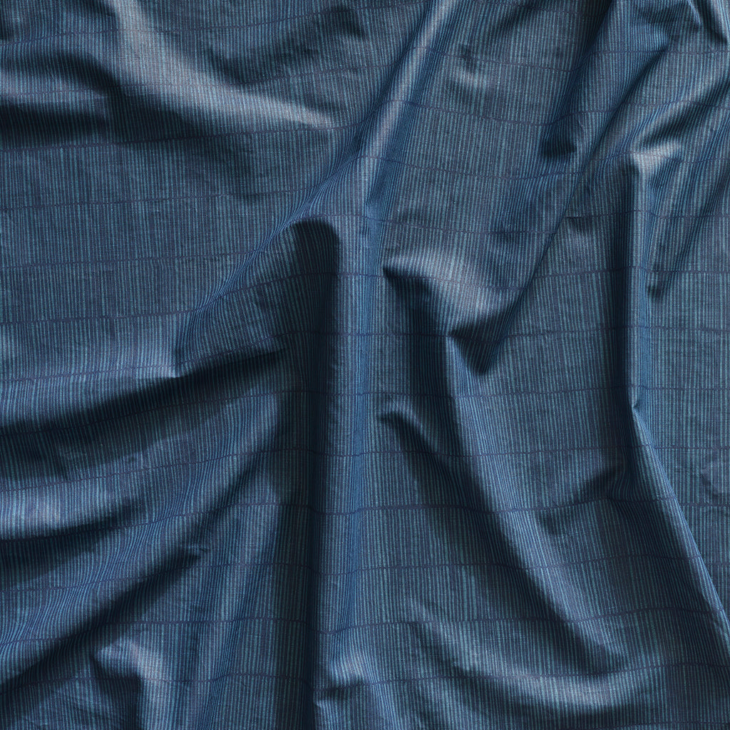 Close up of gently draped printed linen with thin hand drawn stripe grid in dark blue on navy blue.