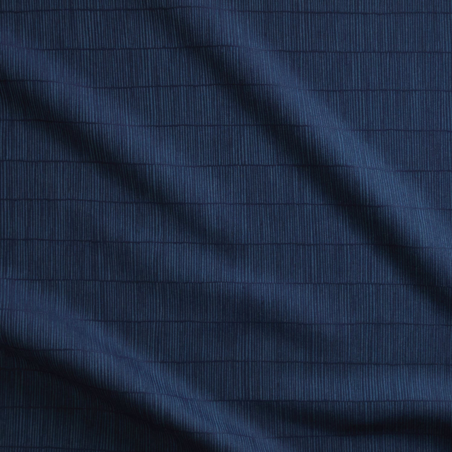 Close up of gently draped woven Indoor-Outdoor fabric with thin hand drawn stripe grid in dark blue on navy.
