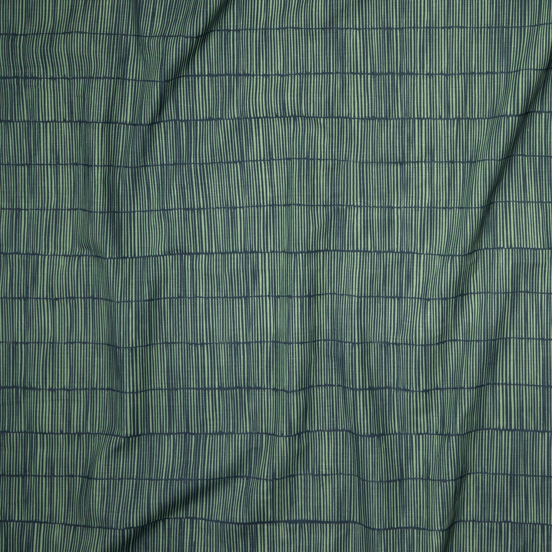 Close up of gently draped printed linen with thin hand drawn stripe grid in green on navy blue.