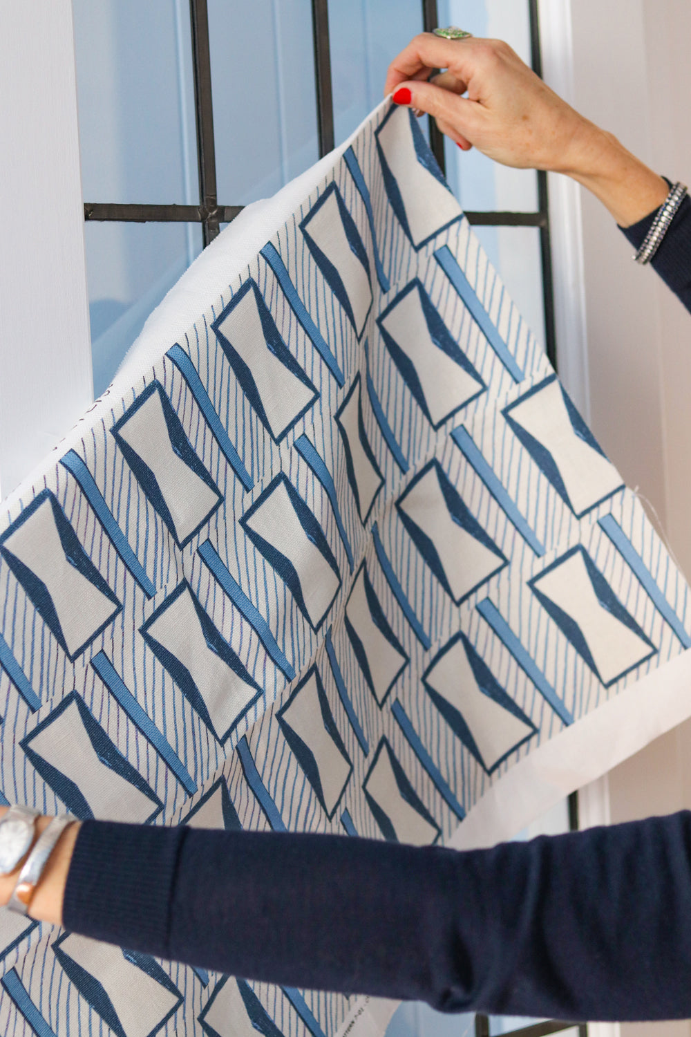 Woman's hands holding a printed fabric cutting with blue and white geometric pattern against a widow. 