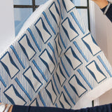 Woman's hands holding a printed fabric cutting with blue and white geometric pattern against a widow. 