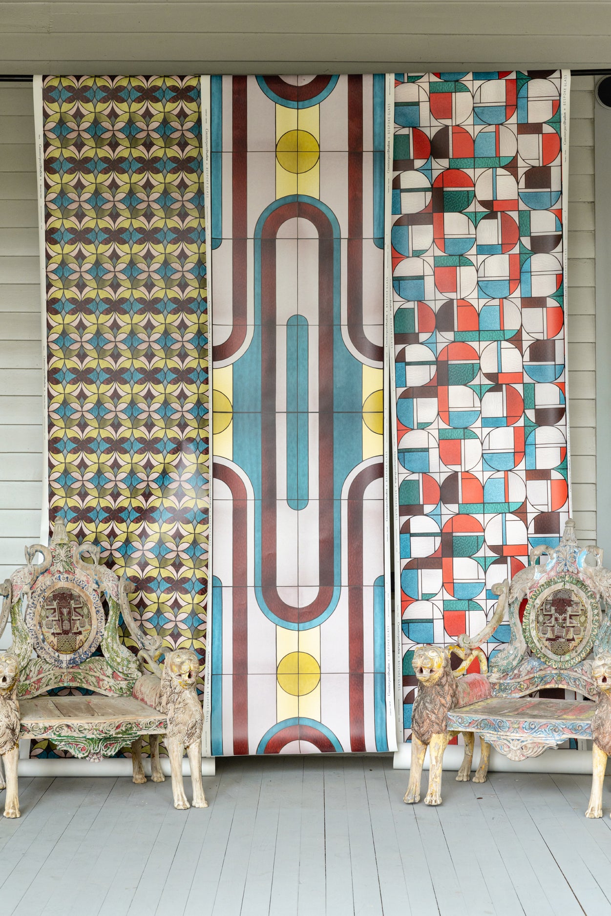 Porch setting with three panels of wallpaper with geometric stained glass patterns and ornate chairs.
