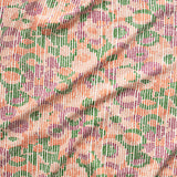 A close up of gently draped printed fabric with a pointillist abstract floral pattern in pink, purple, orange and green on white. 