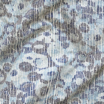 A close up of gently draped printed fabric with a pointillist abstract floral pattern in shades of blue on white. 