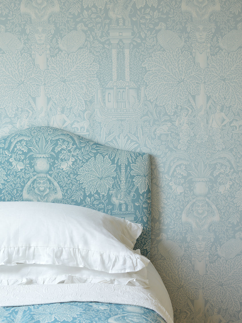 Bed with white bedding and a decorative headboard against a patterned light blue wall.