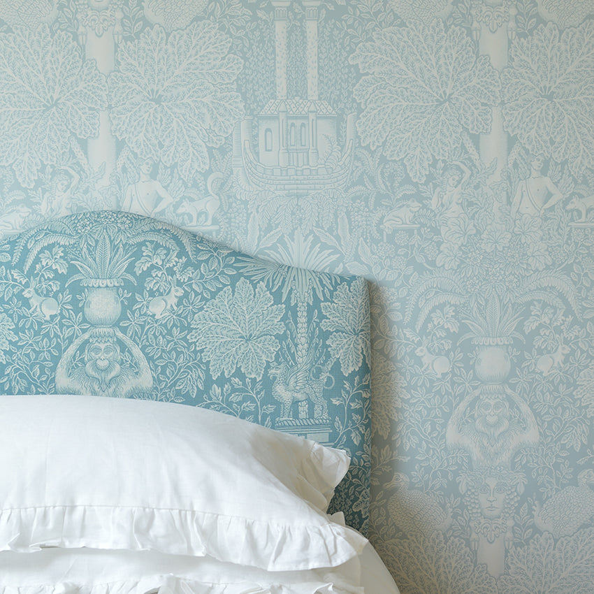 Bed with white bedding and a decorative headboard against a patterned light blue wall.