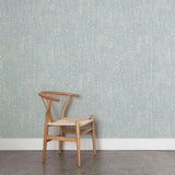 A wooden chair stands in front of a wall papered in a painterly dashed dot print in white on a blue-gray field.